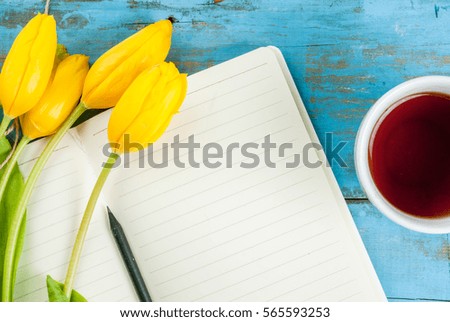 Tea mug with flowers yellow tulips and notebook for notes or wishing on blue rustic table top view, copy space, for Valentine's day