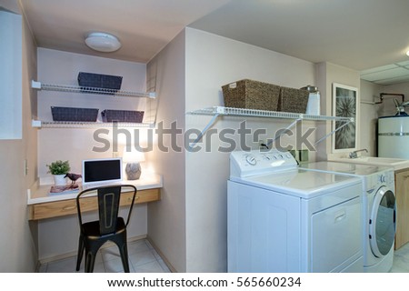 Basement Laundry room interior with work space features a built in desk and white washer and dryer atop tiled floor . Northwest, USA
