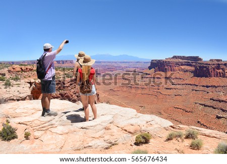 People on hiking trip in the mountains. Father with his family standing on top of the mountain and taking photos of beautiful canyon with smart phones. Canyonlands National Park Utah USA.