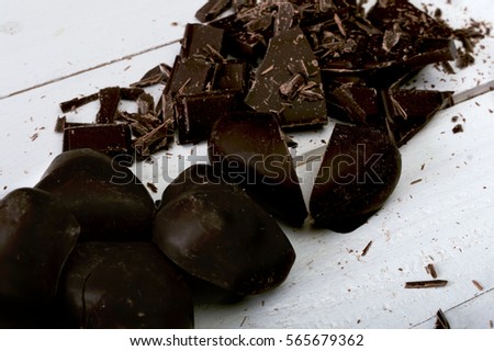 Broken dark chocolate and chocolate hearts on the white wooden table. Selective focus and small depth of field.