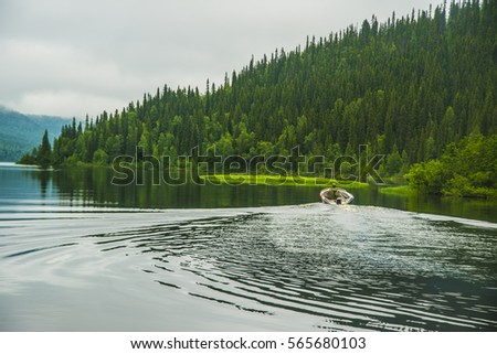 back view. Boat driver was on the back of long boat in speed floating on green forest, mountain and blue water background. 