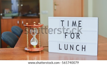 Time for lunch sign in lightbox put on the desk together with hourglass in office interior.