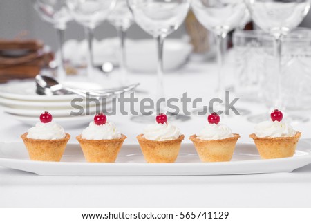 Small tartlets cakes with white cream and red berry on white plate on restaurant table top.