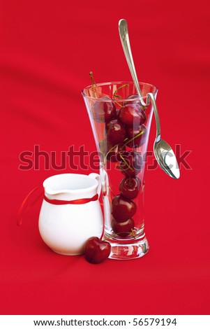 milk jug with a ribbon  glass of cherry and spoon on a red background