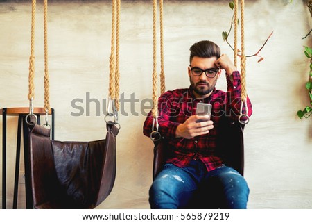 Handsome guy texting someone and sitting on the swing.