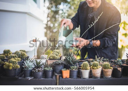 Man watering his cactus. Man taking care of plants at home. Smiling man gardener standing and holding watering can in garden. 