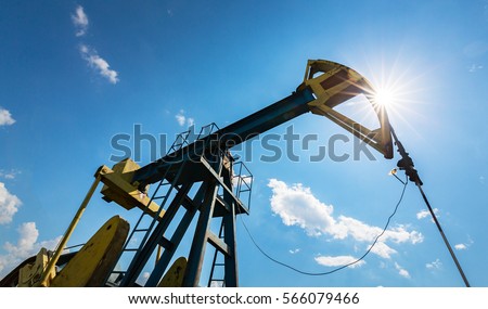 Oil field with pump jack, profiled on blue sky with white clouds, on a sunny day in spring