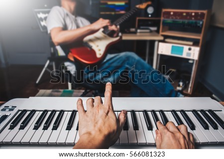 music jamming in sound studio, pianist hands playing keyboard on blurred guitar player background. film filter