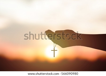 Silhouette rosary against cross in hand. Background sunrise Royalty-Free Stock Photo #566090980