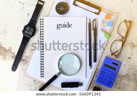 Guide - Top view travel concept of desktop with copy space on paper, glasses, notebook, calculator, pen, pencil, compass and swatch on rustic wooden background.