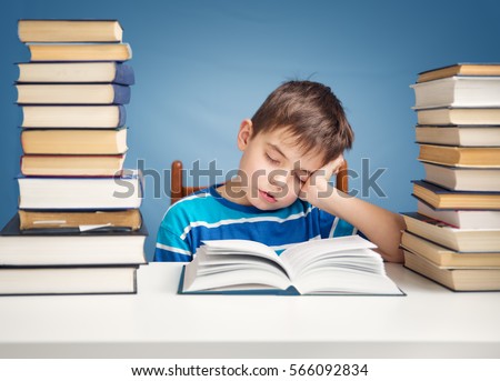 seven years old child reading a book at home. Boy studying at table on blue background