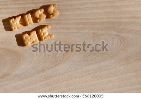 Kiss me. Text from the salty crackers as printed English letters that lie on a wooden chopping board. Message, lined with edible letters