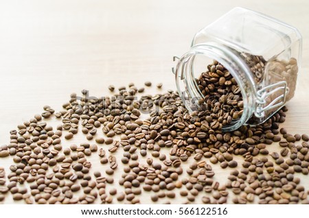 Scattered roasted coffee beans from glass jar on a wooden table - horizontal view