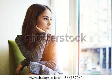 Portrait of mindful attractive young female getting inspired with sunny weather outdoors sitting in modern cafe interior near huge window and copy space area for your advertising looking away Royalty-Free Stock Photo #566157262