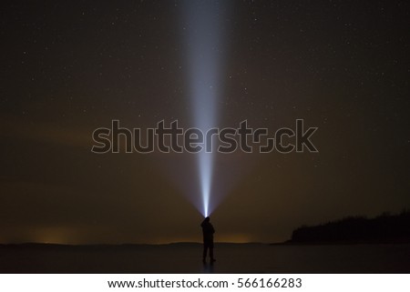 Human standing on ice lake at night in Swedish winter landscape.Shining up in sky with flashlight at stars.Beautiful blue light beam. Nice, calm and peaceful image. Lovely abstract photo.