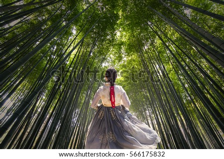 Korean Girl dressed in traditional dress running down path in Bamboo forest Royalty-Free Stock Photo #566175832