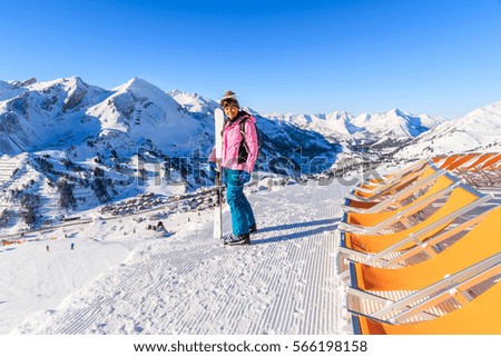 Young woman skier standing near sunchairs and holding skis in Obertauern winter mountain resort, Austria