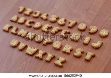 Letters of salty crackers lay on a wooden brown surface in the order similar to the layout of the English alphabet. Funny imitation of the school alphabet using cookies