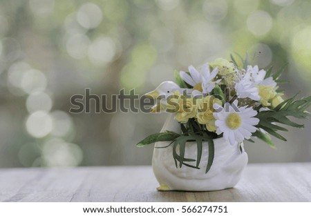 Artificial flowers in a vase on wood and background bokeh.