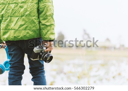 Cute little boy in sweater green holding film camera in the park.