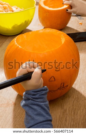 Toddler's hand drawing a face on a pumpkin