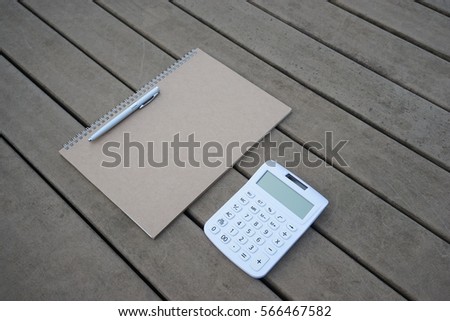 Brown sketch book, pen and white calculator on wooden table.