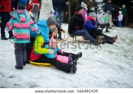 Merry sledging from the hill. At the top of hills crowded. The young woman sits in saucer sled with the little girl and prepares for descent. Another two children near the sled. Cheerful winter.
