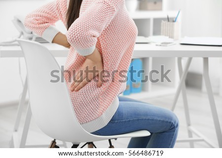 Beautiful young woman suffering from backache in office Royalty-Free Stock Photo #566486719
