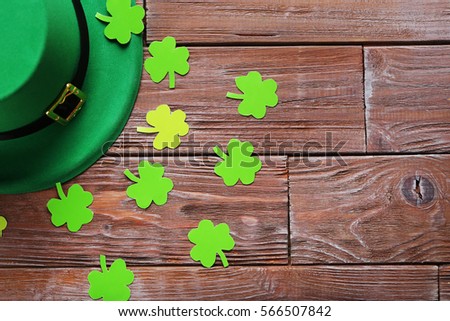 Green paper clover leafs and hat on a brown wooden table