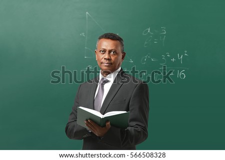 Confident Indian teacher standing near blackboard