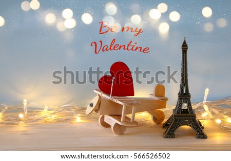 Valentines day background. Wooden plane with heart next to Eiffel Tower on the table. Glitter overlay