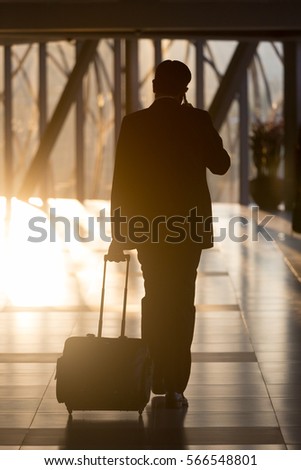 Businessman dragging a small carry on luggage suitcase at airport corridor walking to departure gates.