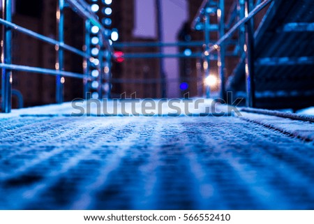 Winter night in the big city, the snow-covered staircase with lantern on the background of skyscrapers. Close up view from the staircase level, image in the blue tones