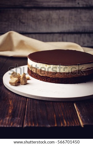 delicious three-layer chocolate cake stands on a circular base, lying next to rushy sugar and tongs on a wooden table and dark background. place for text. food design.