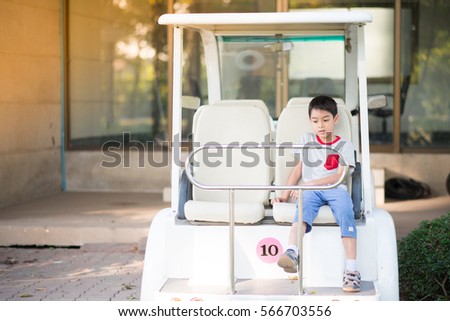 Little boy sitting behind the golf carts in the park 