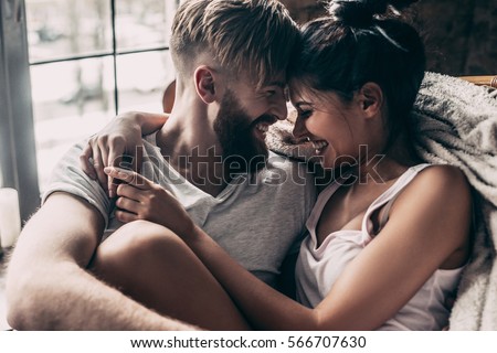 Love you so much! Beautiful young couple smiling and sitting face to face in chair while spending time at home together