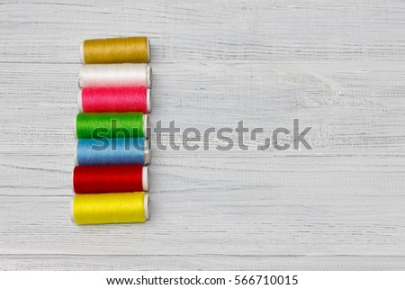 Bobbins with colorful threads on old wooden table background.