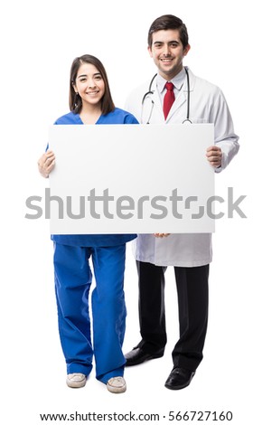 Full length view of a young doctor and a nurse holding a white blank sign in a studio and smiling