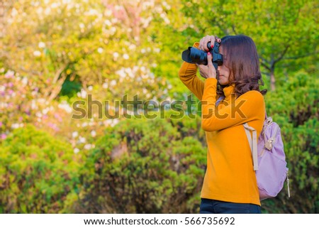 Happy woman traveler take photos by camera with cherry blossoms tree on vacation while spring with blurred background, Soft focus