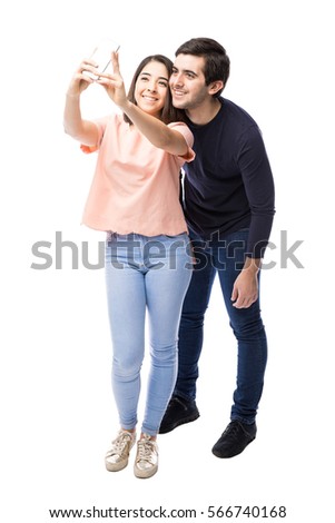Full length portrait of a good looking young couple taking a selfie with a smartphone