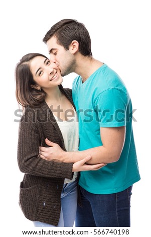 Pretty girl getting a kiss on the cheek from her boyfriend and smiling on a white background