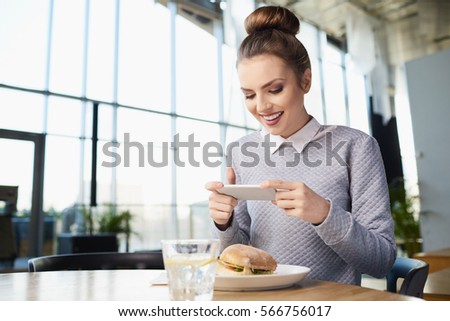 Smiling woman in cafe taking picture of her food with smartphone and smiling. Copy space