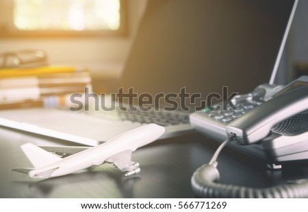 Online Travel Agency operator office desk set up with plane laptop telephone. Business travel trip concept. Royalty-Free Stock Photo #566771269