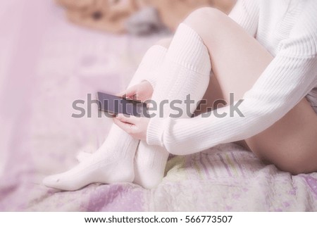 Soft photo of woman sitting on bed with a cell phone.