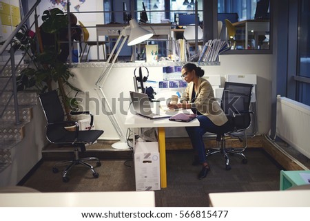 Young female talented administrative manager working with financial documents and reports organizing them into folder in database using computer and wireless connection in company headquarter indoor