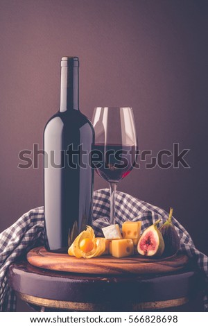 Red wine. Romantic composition from a wine bottle, glass of wine, an appetizer of hard cheese, brie cheese, figs and physalis. Postcard greetings.