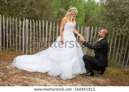 married couple outdoors, the groom kneeling in front of his wife