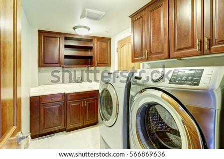 Laundry room interior with modern steel appliances, wood cabinets with sink and marble tile floor. Northwest, USA