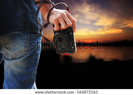 Man holding camera in hand on sunset nature background