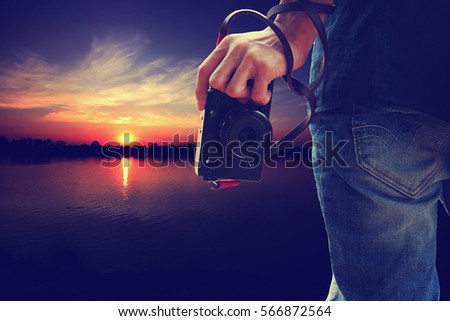 Man holding camera in hand on sunset nature background